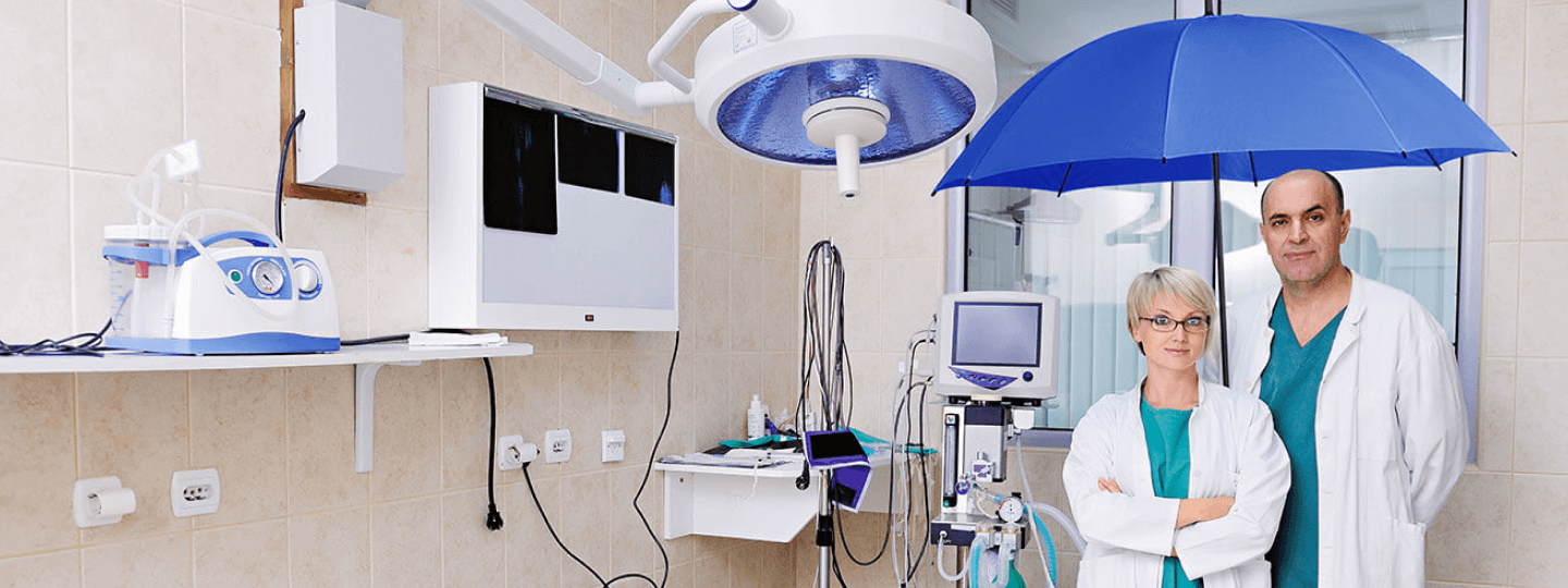 Mann und Frau aus dem Gesundheitsbereich im Behandlungszimmer unter dem blauen Schutzschirm