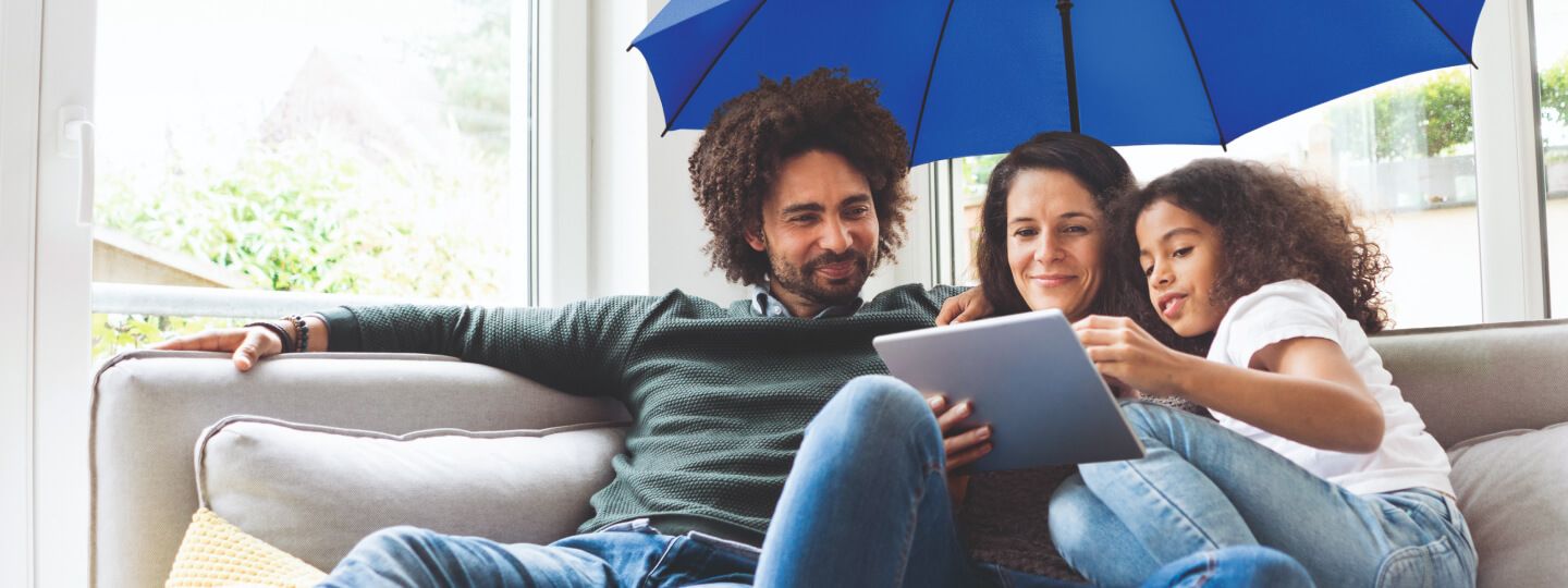 Familie sitzt auf dem Sofa mit blauem Schirm über sich und schaut in ein Tablet