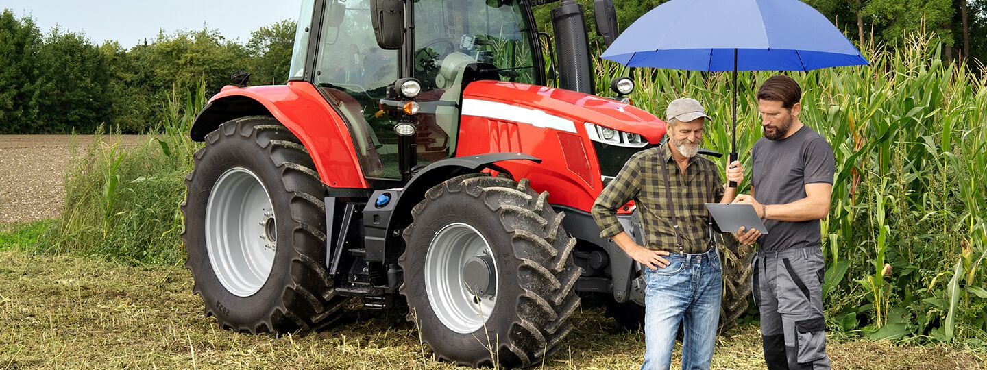 Zwei Männer unter dem blauen Schutzschirm stehen vor einem Traktor auf dem Feld.