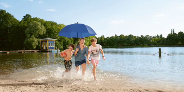 Frau mit zwei Kindern und blauem Schirm über ihnen am Strand
